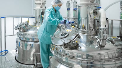 Gowned operator working at bioreactor vessels in a GMP manufacturing suite