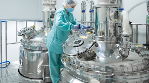 Gowned operator working at bioreactor vessels in a GMP manufacturing suite